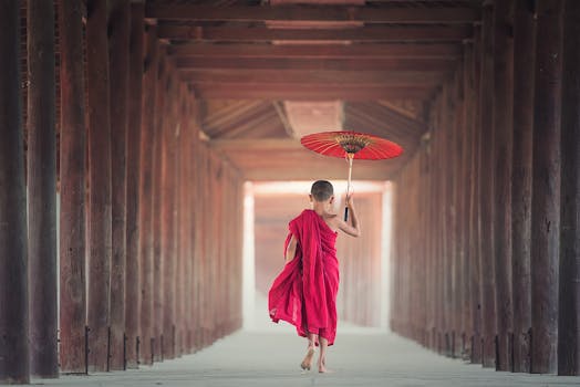 A child monk holding a parasol walks through a traditional Asian temple corridor, embracing cultural heritage.