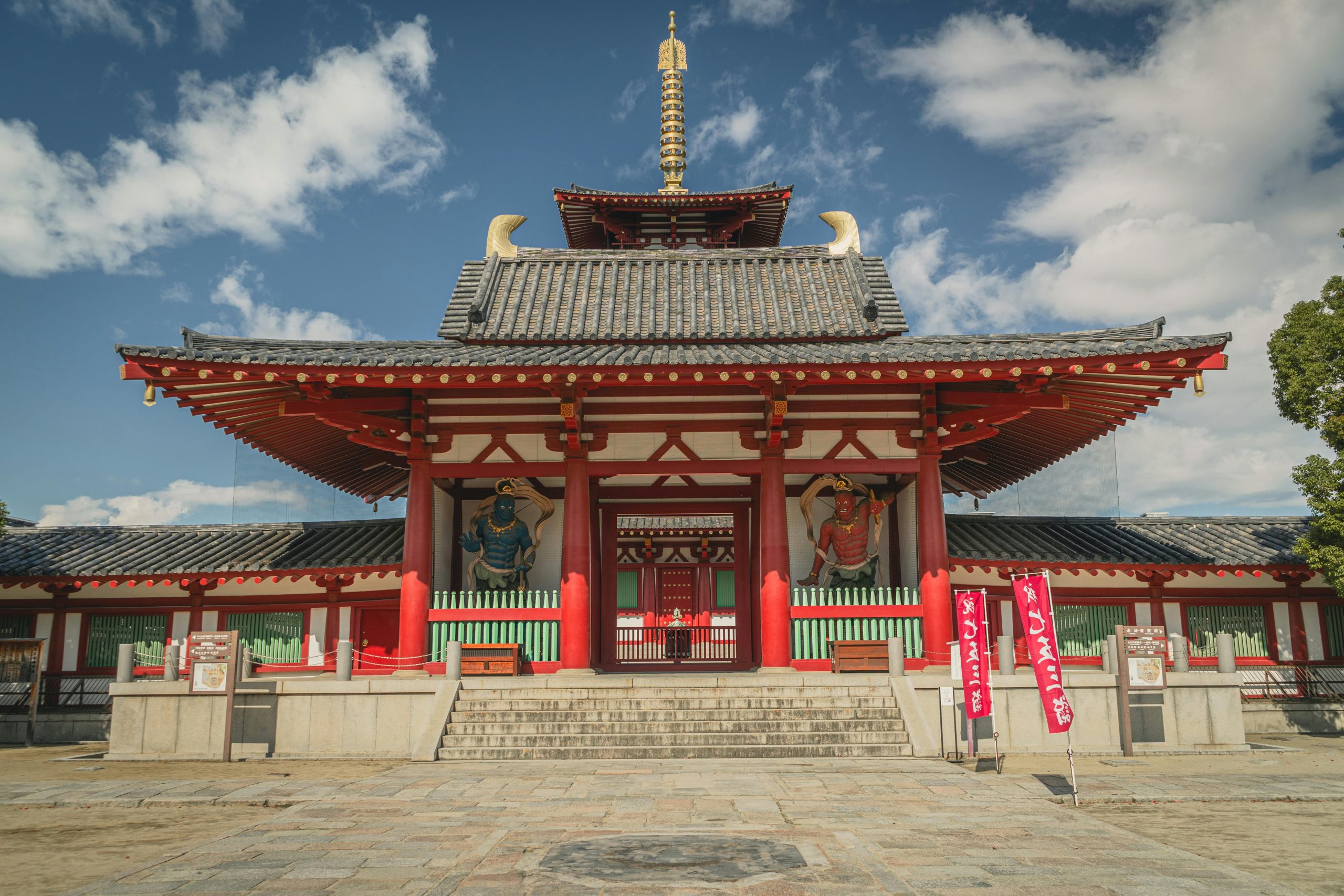 Front view of Shitennoji Temple with vibrant red architecture in Osaka, Japan, under a clear sky.