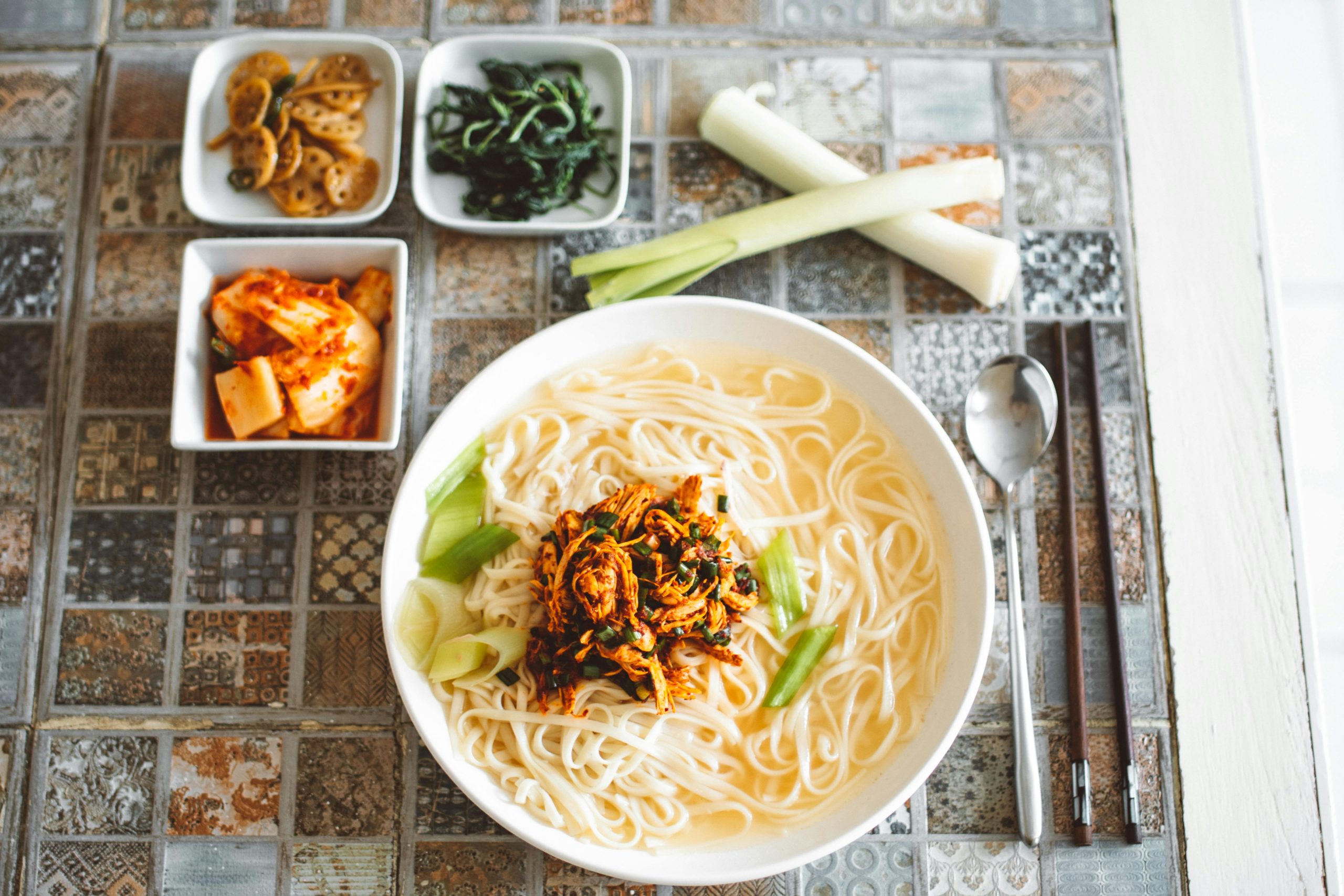 Authentic Korean noodle soup served with kimchi and side dishes on a patterned table.